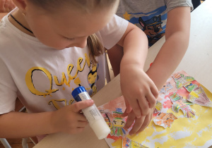 dziewczynka i chłpiec przyklejaja na karton ilustracje wioski indiańskiej