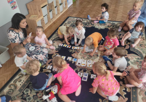 Dzieci siedza na dywanie i razem z panią nazywają obrazki.