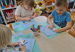 Dzieci kolorują kartę pracy na któej są kalosze