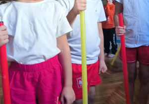 Dzieci stoją trzymając w rękach laski gimnastyczne