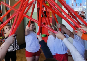 Dzieci trzymają laski gimnastyczne stykając się końcami