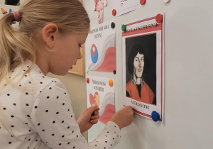 Dziewczynka przyczepia na tablicy ilustrację Mikolaja Kopernika