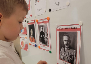 Chłopiec przyczdepia na tablicy ilustrację Józefa Piłsudzkiego