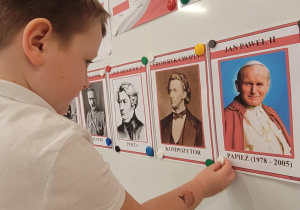 Chłopiec przyczepia na tablicy ilustrację Jana Pawła II