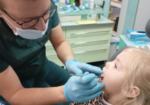 Dziewczynka siedzi na fotelu dentystycznym i pokazuje zęby