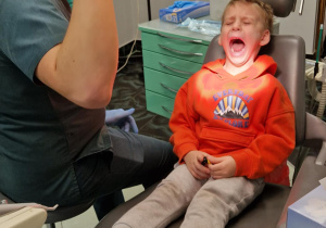 Chłopiec siedzi na fotelu dentystycznym a pan doktor ustawia lampę