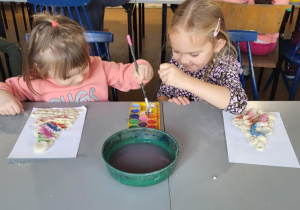 Dziewczynki nabierają farbe na pędzelki, aby pomalować choinkę z masy solnej