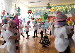 Dzieci idą po kole z kolorowymi miotełkami