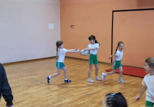 Dziewczynki w kole podają sobie piłkę do ragby