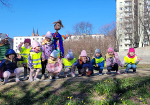 dzieci z kukłą Marzanny kucają oglądając kwiaty