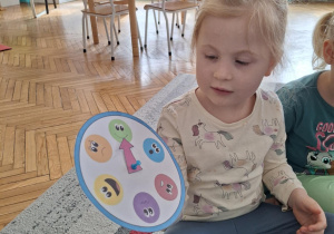 Dziewczynka na zegarze emocji wskazuje emotkę radości