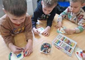 Chłopcy maluja pastelami papierowe jajka