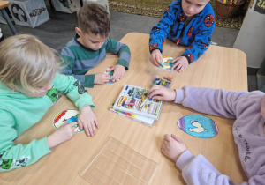 Dzieci siedzą przy stole i malują papierowe jajka
