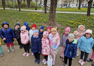 Dzieci stoją na tle wiosennych kwiatow w parku