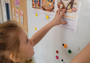 Dziewczynka przyczepia planszę z koszyczkiem wieklanocnym na tablicę