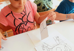 dziewczynka siedzi przy stoliku i układa puzzle, na których widnieje postać dziecka