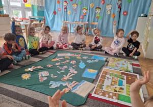 Dzieci siedza na dywanie przed ilustracjami wakacyjnymi