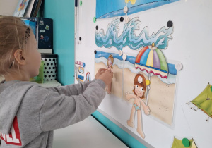 Chłopiec przyczpia do tablicy sylwetę chłopca na plaży