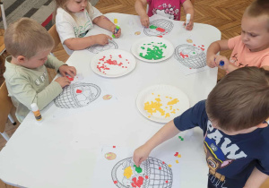 Dzieci przy stoliku wyklejają kosz z owocami
