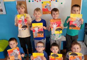 chłopcy prezentują pracę plastyczną "Na sawannie" wykonana farbami i naklejoną sylwetą zebry oraz żyrafy w kolorach czarnobialych