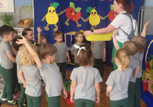 dzieci stoją przed dekroacją z jabłkami i gruszkami i napisem owoce