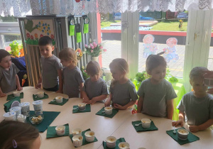 dzieci stoją wokół stołu i degustują jogurt z bananami