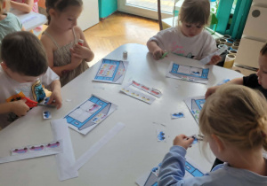 Dzieci siedza przy stole i wycinają pojazdy
