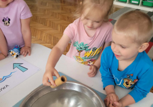 Dziewczynka wklada do miski drewnianą rurkę