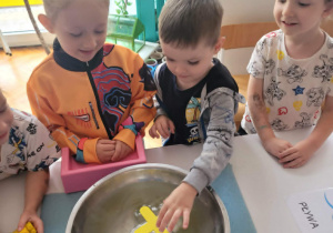 Chlopiec wkłada do miski z wodą drewniany iks