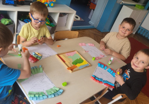 chłopcy siedzą przy stole skladaja kolorowe paski i przyklejają na szablon motyla