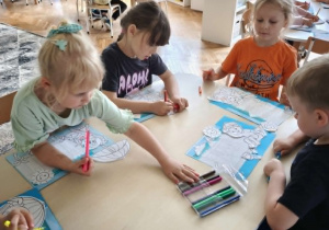 Dzieci siedzą przy stoliku z praca plastyczną