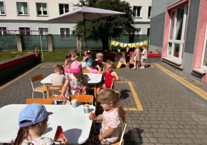 Dzieci siedza przy stolikach na tarasie przedszkolnym