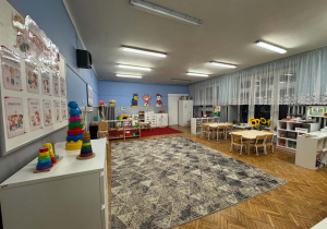 sala przedszkolna ze stolikami, zabawkami i dywanem