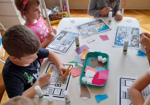 dzieci przy stoliku naklejają kolorowe skrawki kartek na makietę ulicy