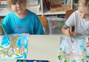 Dzieci siedzą przy stoliku i malują farbami