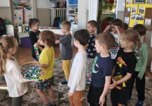 Chłopcy idą w kole, dziewczyna podaje im prezenty
