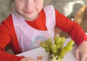 dziewczynka ma przed sobą jeża z winogrona
