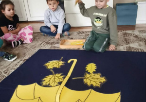 dzieci siedzą przed parasolem z kartonu