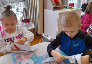 dzieci wycinają śnieżynki i przyklejają na kartkę papieru obok sylwety Mikołaja