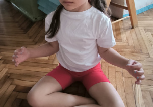 dziewczynka siedziw siadzie skrzyznym ręce ma rżłozone na bok i stabilizuje oddech