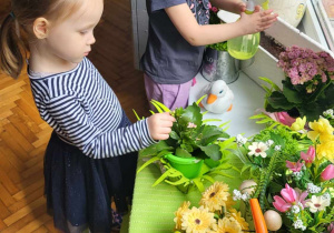 dwie dziewczynki zraszają doniczki z kwiatami wodą
