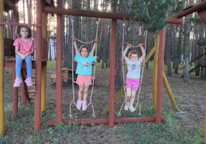 dwie dziewczynki wspinają się po drabinkach ze sznurka a trzecia dziewczynka siedzi obok drabinek