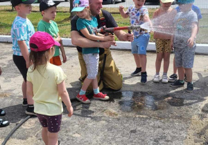 dziewczynka ze strażakiem leje wodę z węża strażackiego