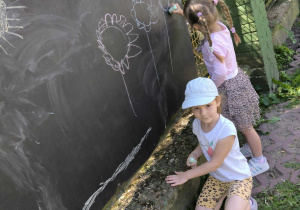 dwie dziewczynki rysują na tablicy kredą kolorowe kwiaty