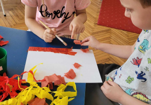 dzieci przyklejają czerwoną bibułe za pomocą wody do kartki