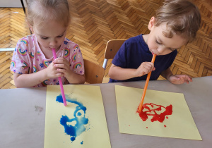 chłopiec i dziewczynka rozdmucjują niebieską i czerwoną farbę na kartce