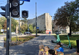 Dzieci stoją przy skrzyżowaniu i obserwują ruch drogowy