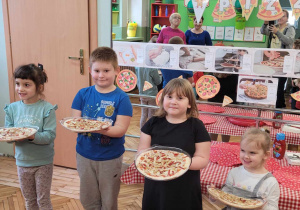 czwórka dzieci stoi na tle dekoracji na lustrze z nieupieczoną pizzą w rękach