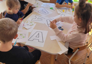 Dzieci przy stoliku wykonują kartę pracy z literą A