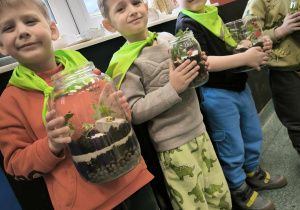 czterech chłopców stoi prezentuje swoje kompozycje roślinne w szkle